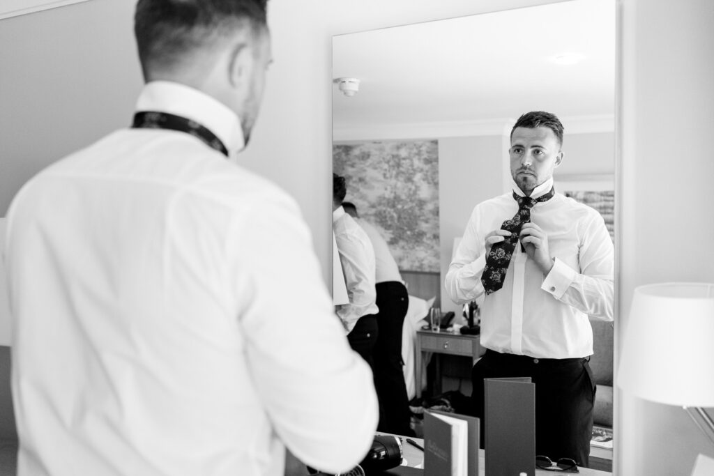 Groom getting ready in mirror at Ellie and Sam's Rhinefield House Hotel wedding in the New Forest