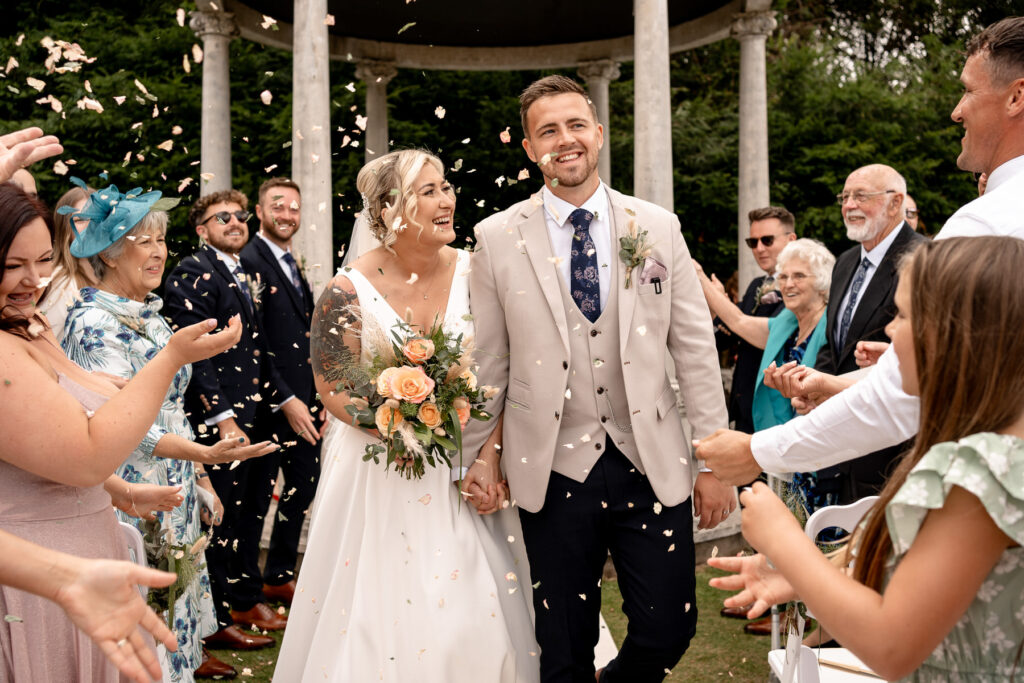 Bride and Groom walking through confetti laughing at Rhinefield House Hotel
