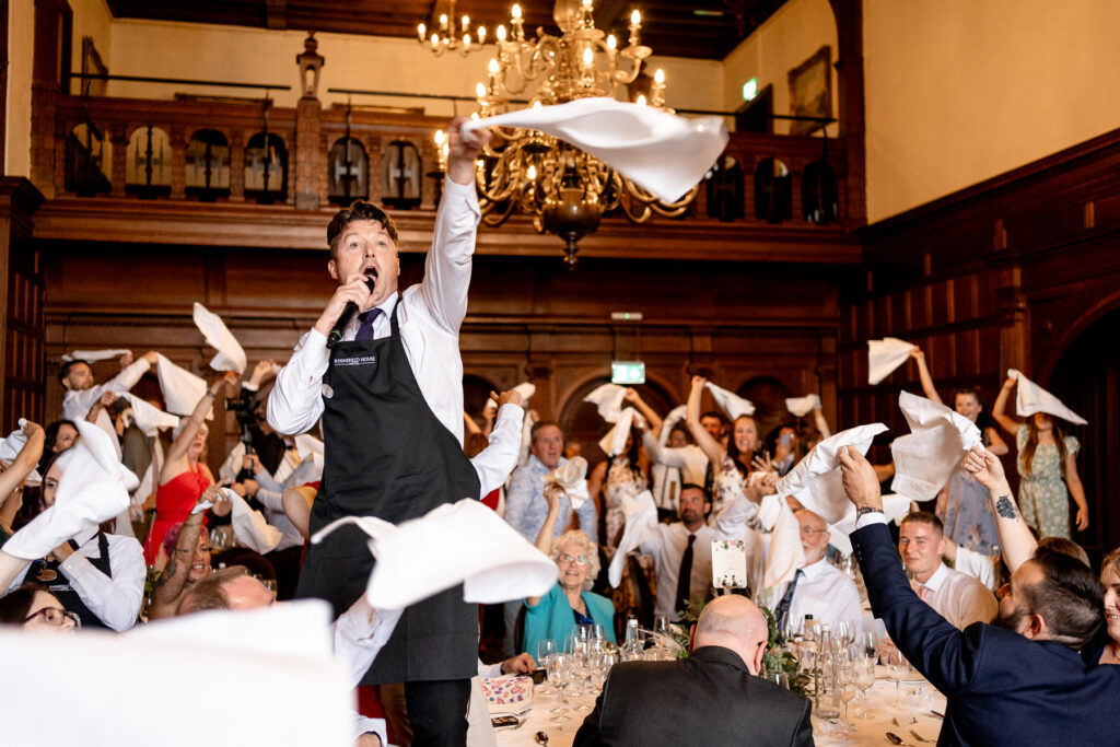Rhinefield House Hotel Wedding photographer for Ellie and Sam - surprise singing waitors napkin waving